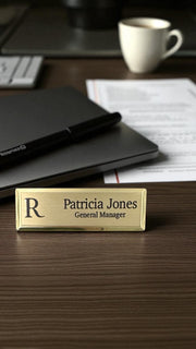 Gold name tag with name and title on a desk with office supplies.