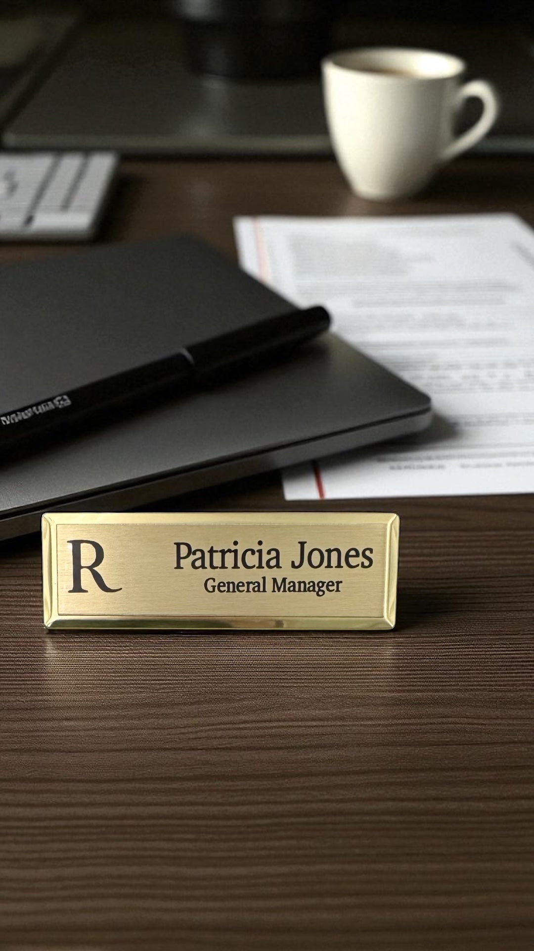 Gold name tag with name and title on a desk with office supplies.